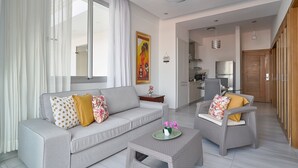 Ein modernes Wohnzimmer mit einer Couch, zwei Sesseln, einem Couchtisch und einem Essbereich mit einer Küche im Hintergrund.