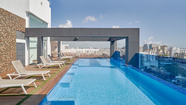 Ein Rooftop-Endlospool mit Liegestühlen und Blick auf die Stadt.