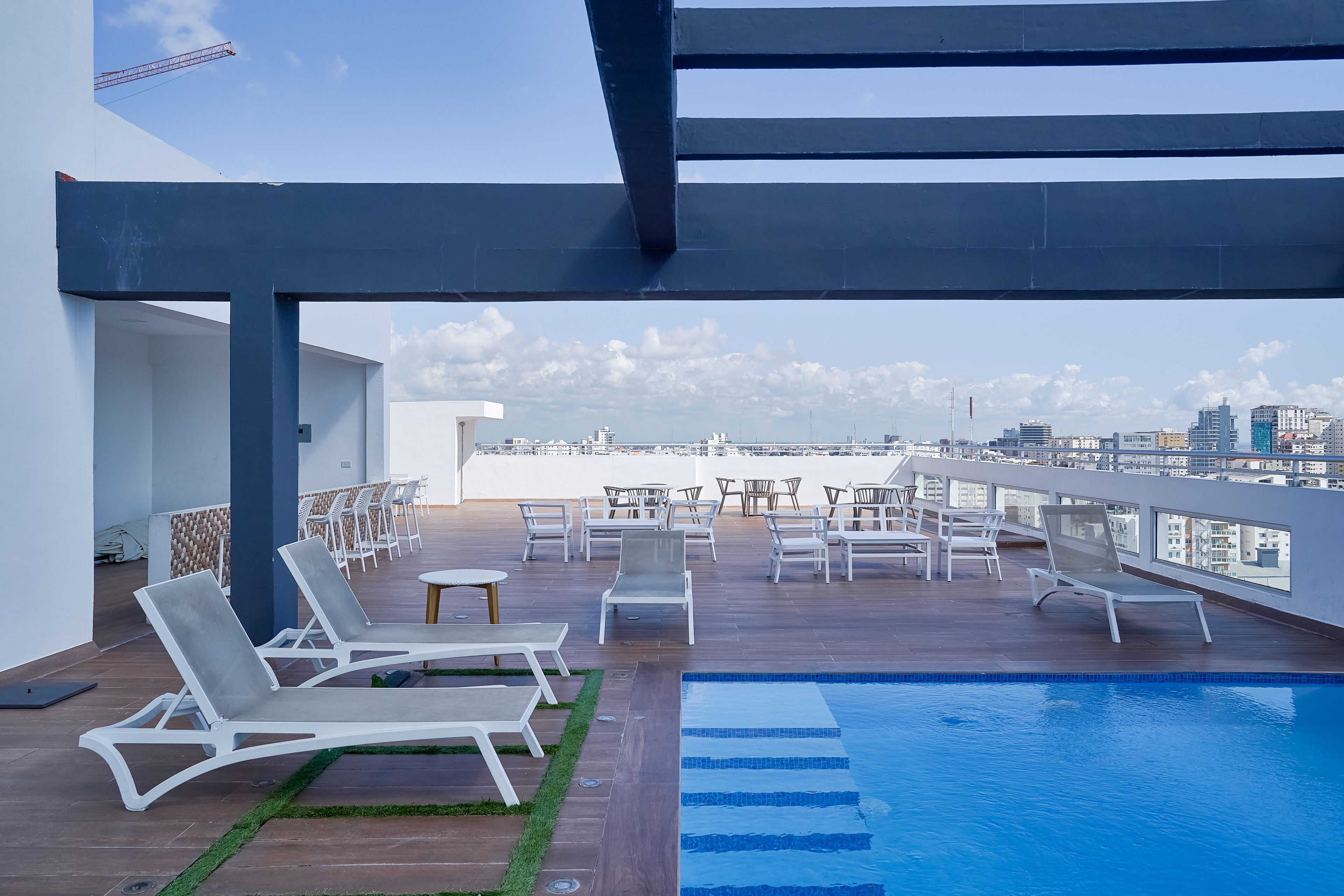 Un área de piscina en la azotea con sillones y mesas, vistas despejadas del horizonte de la ciudad y un diseño arquitectónico moderno.