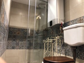 Une salle de bain équipée d’une douche, de toilettes et d’un mur recouvert de carreaux formant un motif décoratif.