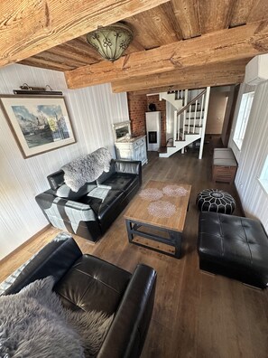 Un salon spacieux avec un canapé en cuir noir, une table basse en bois et un escalier menant à un autre niveau.