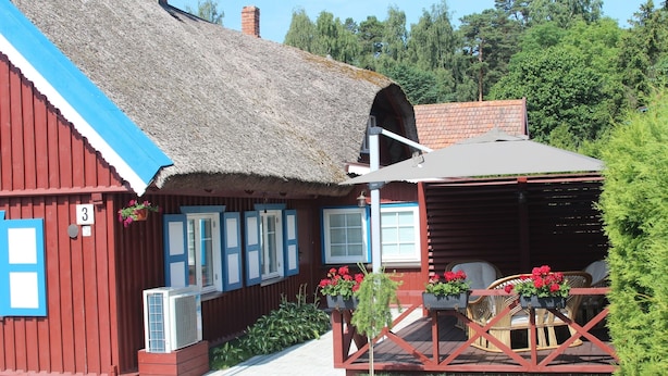 A rustic wooden building with a thatched roof, a covered outdoor seating area with wicker furniture, and a small garden with potted plants.