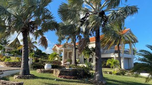 A resort with palm trees, a white building with a red roof, and a garden with a large white pot. - Sea Views Villa & Guest House with 2 Private Pools. In a Private Club (St. Paul's)