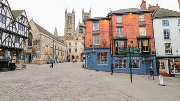 A cobblestone square with historic buildings, including a pub named 'Magna Carta' and a church with a tall spire in the background.