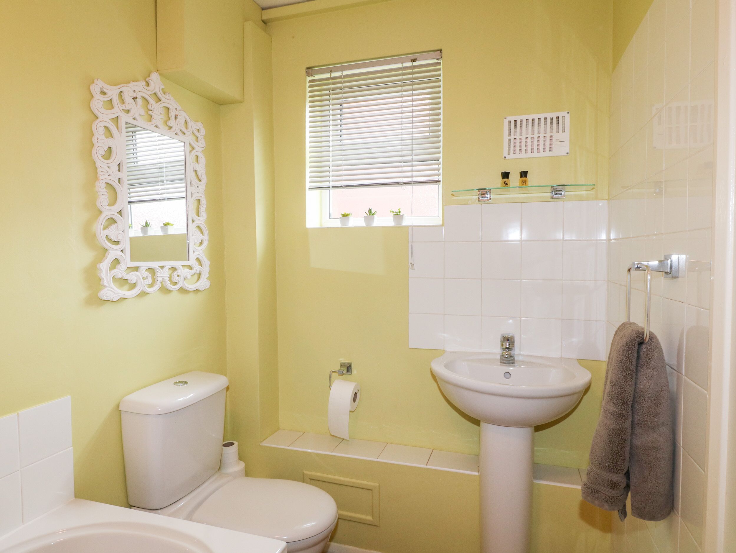 A bathroom with a toilet, sink, and window with blinds.