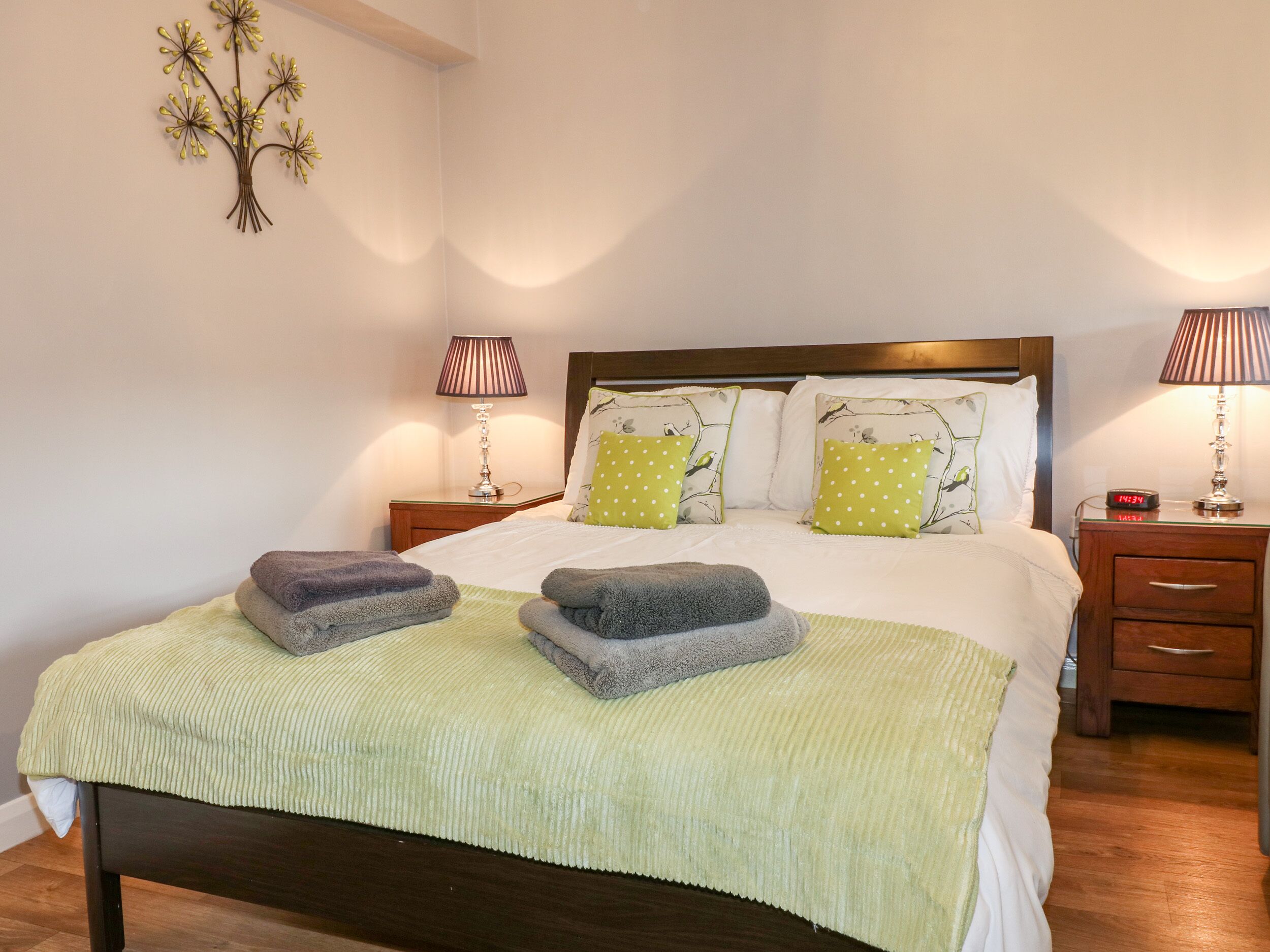 A neatly made bed with two pillows, a bedside table with a lamp, and a wall decoration.