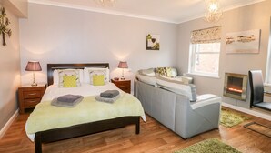 A well-lit bedroom with a bed, bedside tables, a sofa, a fireplace, and artwork on the walls. - Grayz Studio (Lincoln)