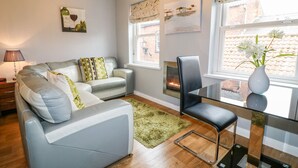 A modern living room with a grey sofa, a glass coffee table, and a fireplace. - Grayz Studio (Lincoln)