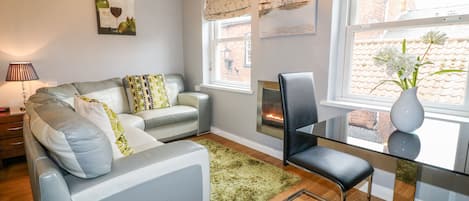 A modern living room with a grey sofa, a glass coffee table, and a fireplace.
