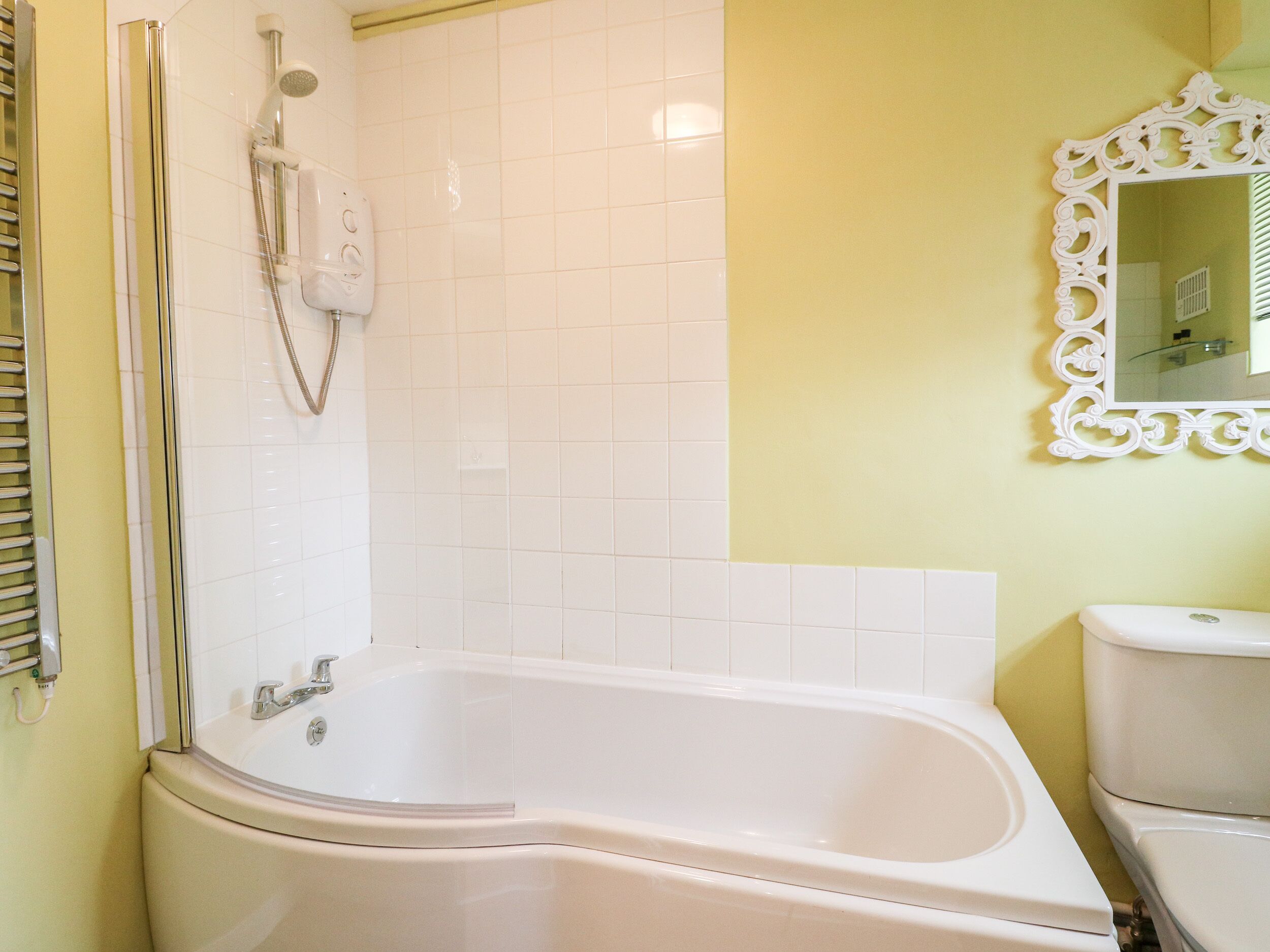 A bathroom with a white bathtub, a toilet, and a shower with a handheld showerhead.