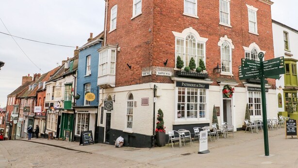 A traditional brick building with a sign for 'Patisserie & Deli' and a signpost indicating nearby attractions. - Grayz Studio (Lincoln)