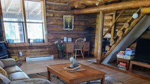 A cozy log cabin interior with a wooden ceiling, a fireplace, a sofa, a coffee table, and a TV.