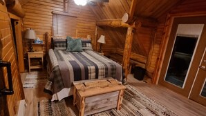 A cozy attic bedroom with a wooden ceiling, a bed with plaid bedding, a small wooden bench, and a patterned rug.