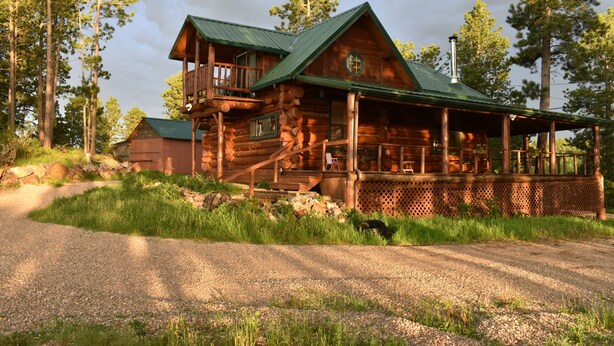 A log cabin with a balcony, a porch, and a chimney.
