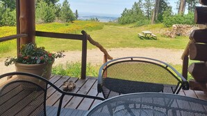 A wooden deck with a table and chairs, overlooking a grassy area with trees and a distant view.
