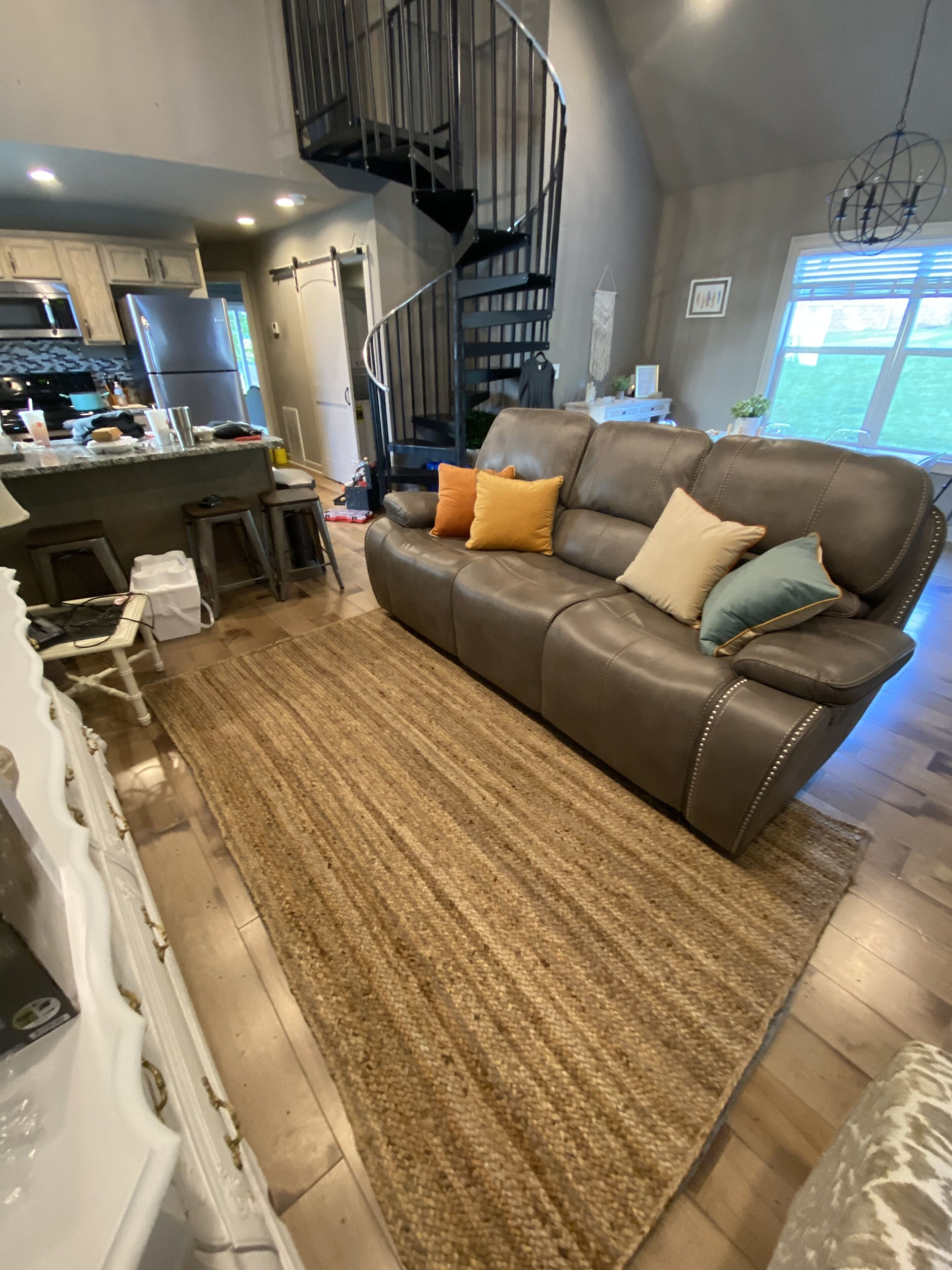 A modern kitchen with a built-in refrigerator, a dining area with a bar stool, and a living room with a leather sofa and a patterned rug.