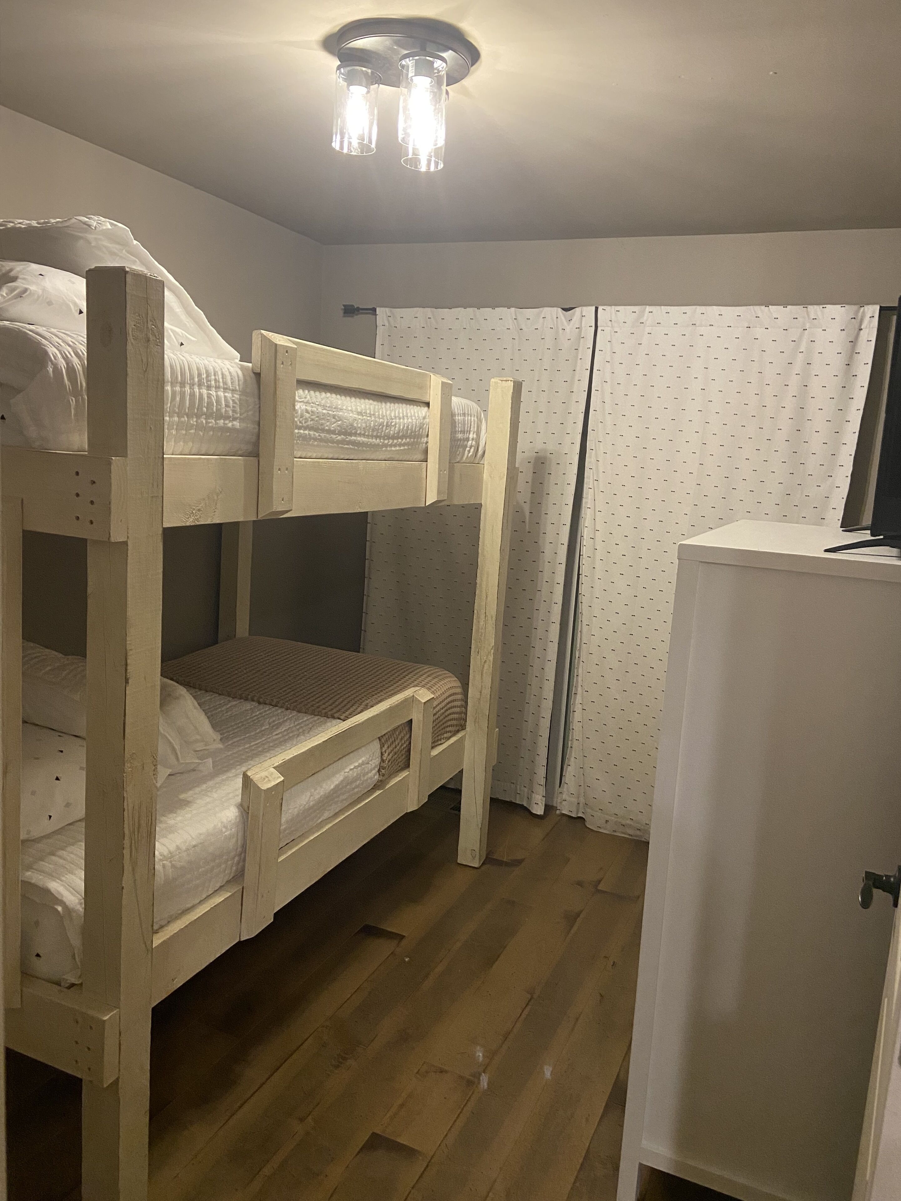 A bunk bed with a wooden frame, a white cabinet, and a ceiling light fixture.