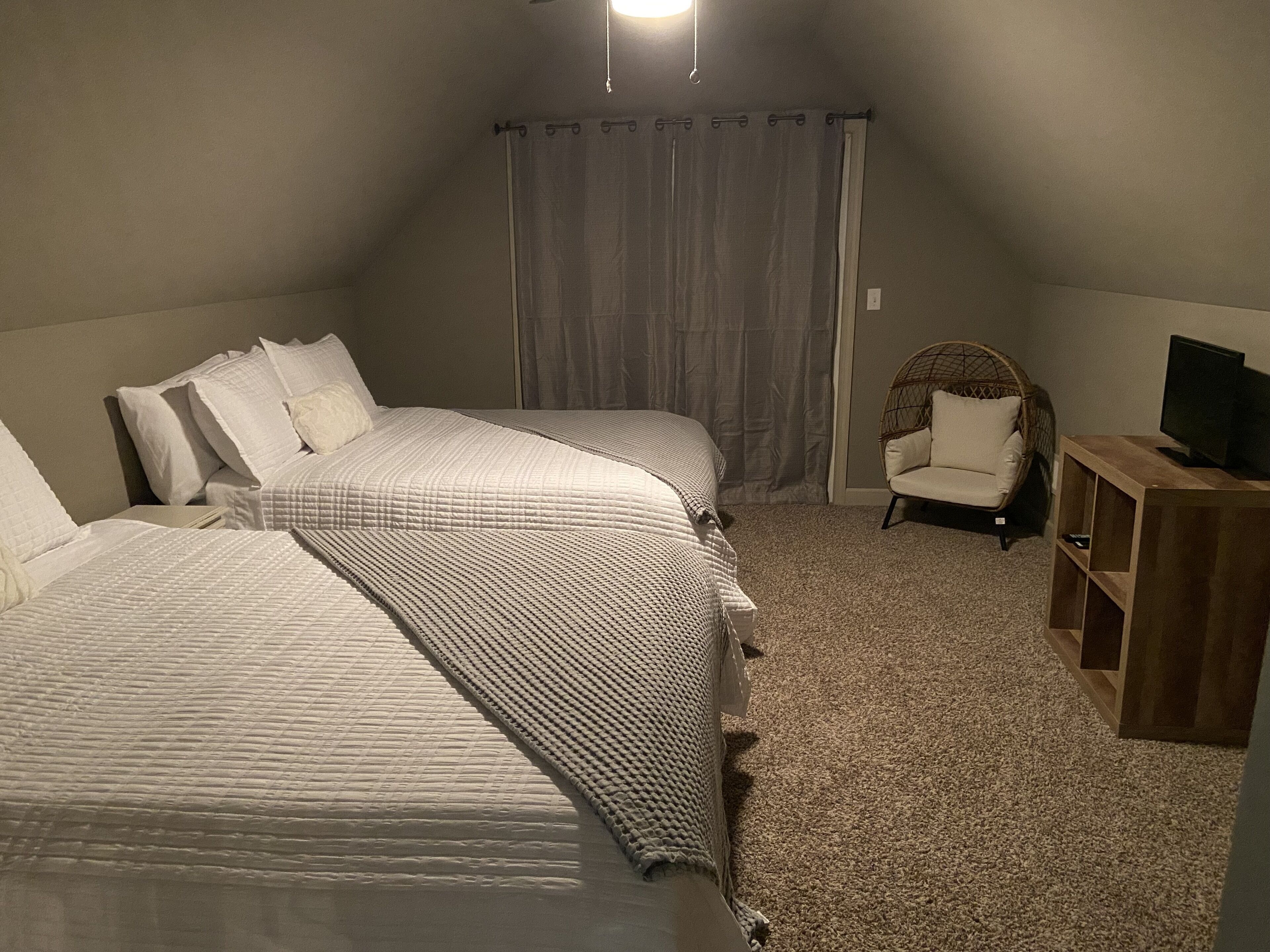 A bedroom with two beds, a chair, a TV stand, and a curtain.
