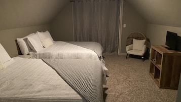 A bedroom with two beds, a chair, a TV stand, and a curtain.