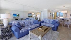 Una sala moderna con dos sofás azulados estampados, una mesita redonda y un comedor con una mesa y sillas blancas.