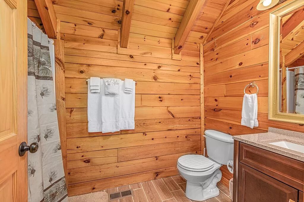 A wooden cabin bathroom with a toilet, sink, and towel rack.