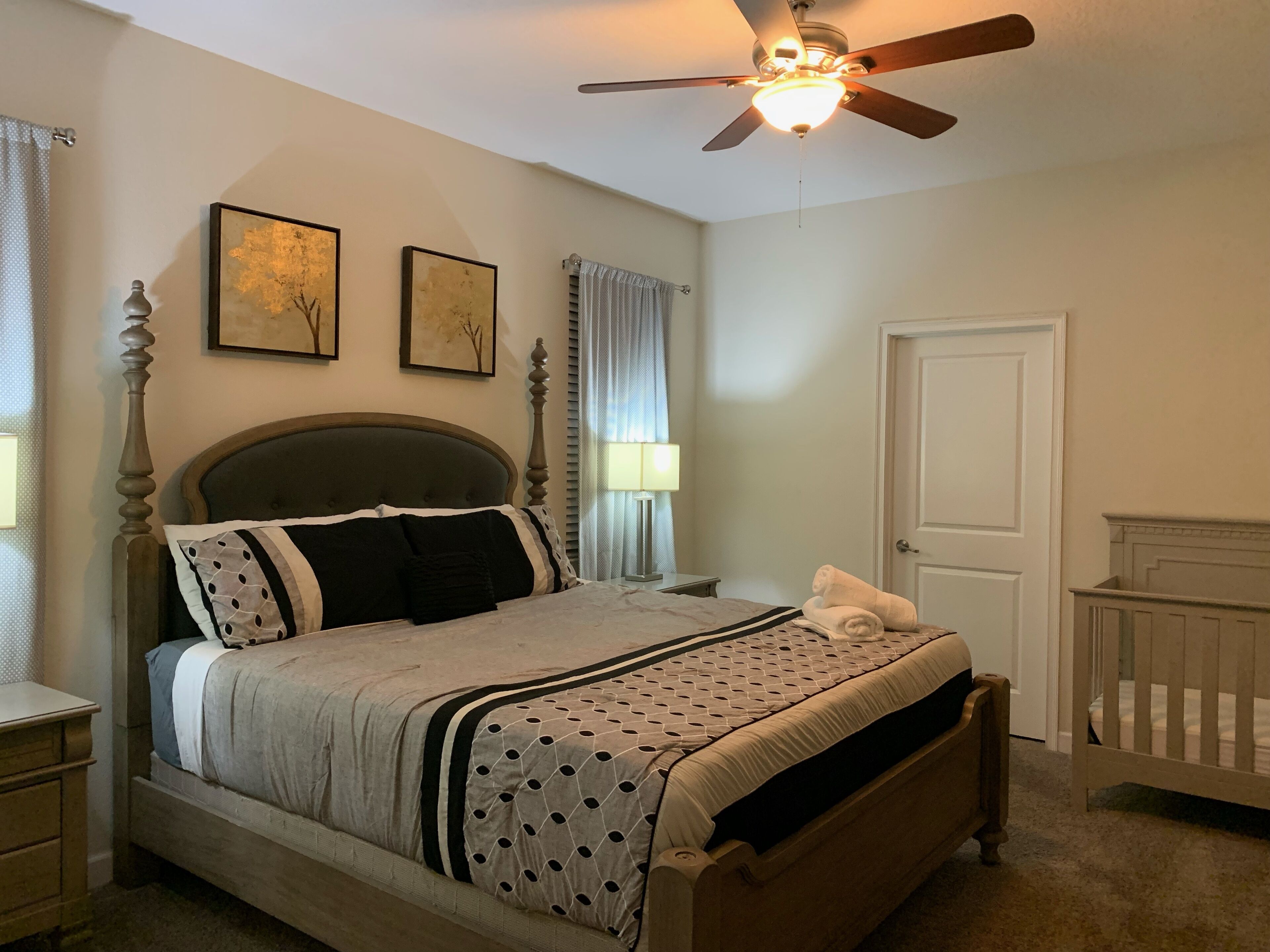 A bedroom with a bed, a ceiling fan, a door, and two framed pictures on the wall.