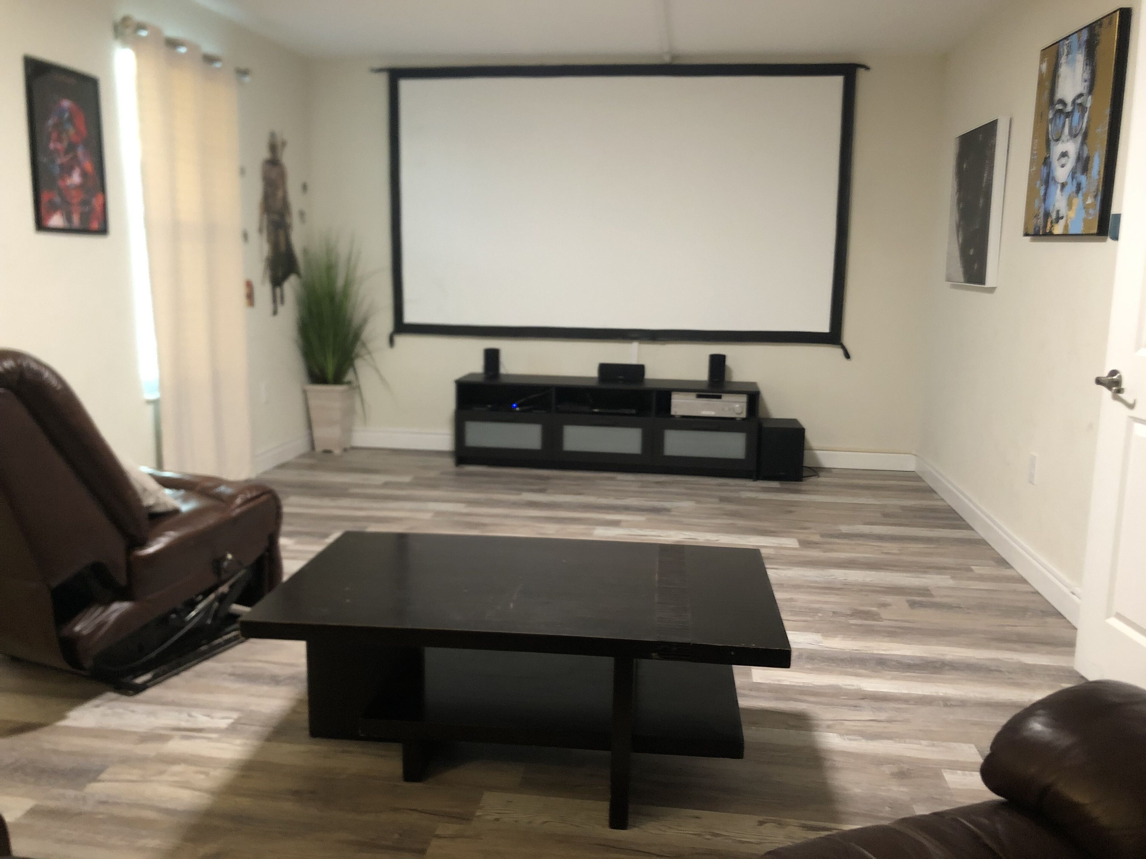 A living room with a black coffee table, a brown leather sofa, a TV on a black stand, and a projector screen.