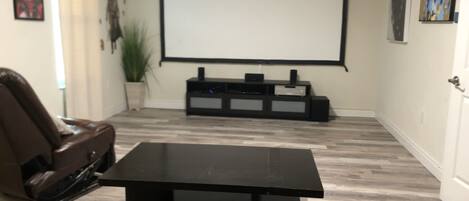 A living room with a black coffee table, a brown leather sofa, a TV on a black stand, and a projector screen.