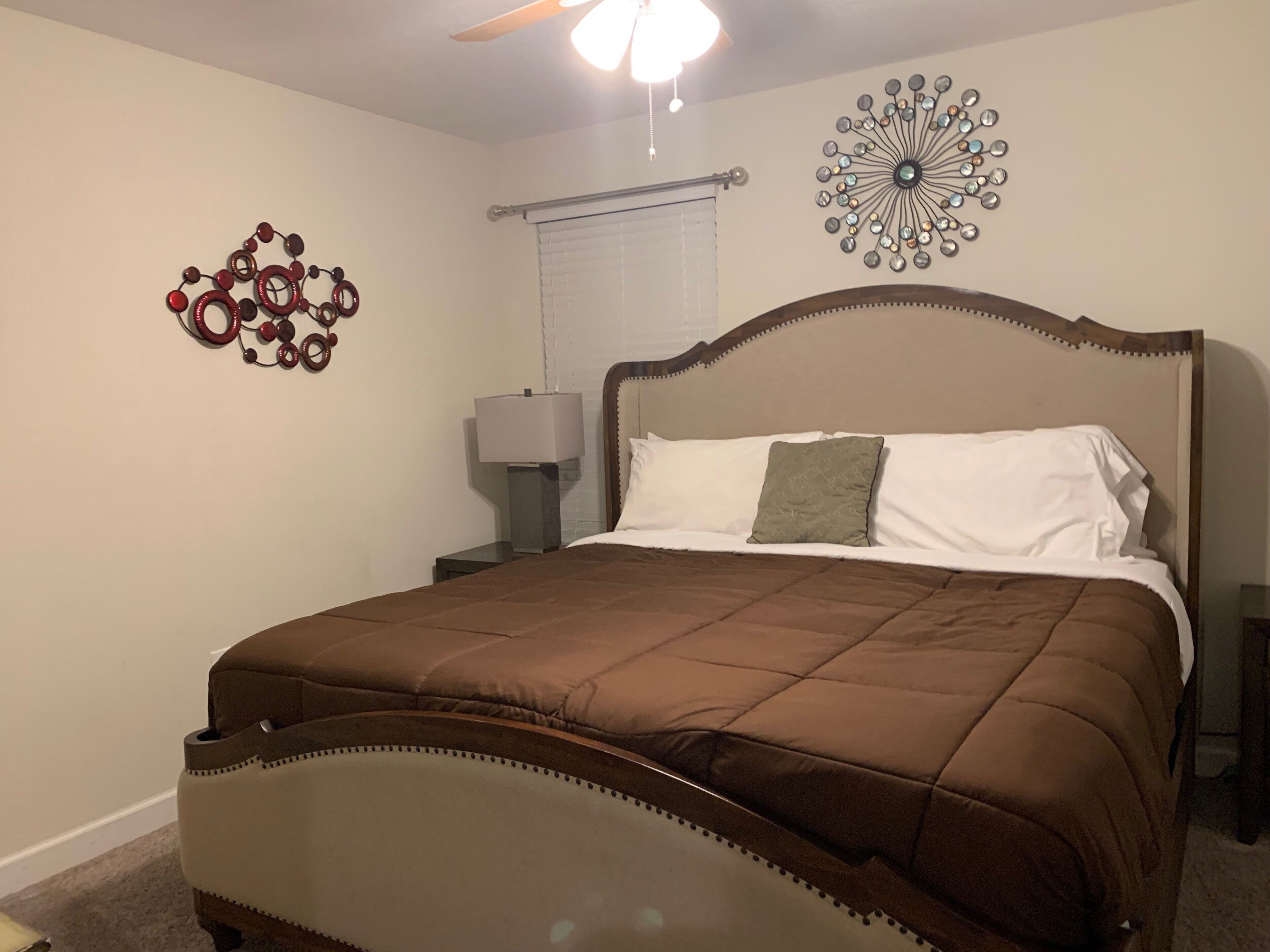 A bedroom with a bed, a nightstand, a lamp, and decorative wall art.