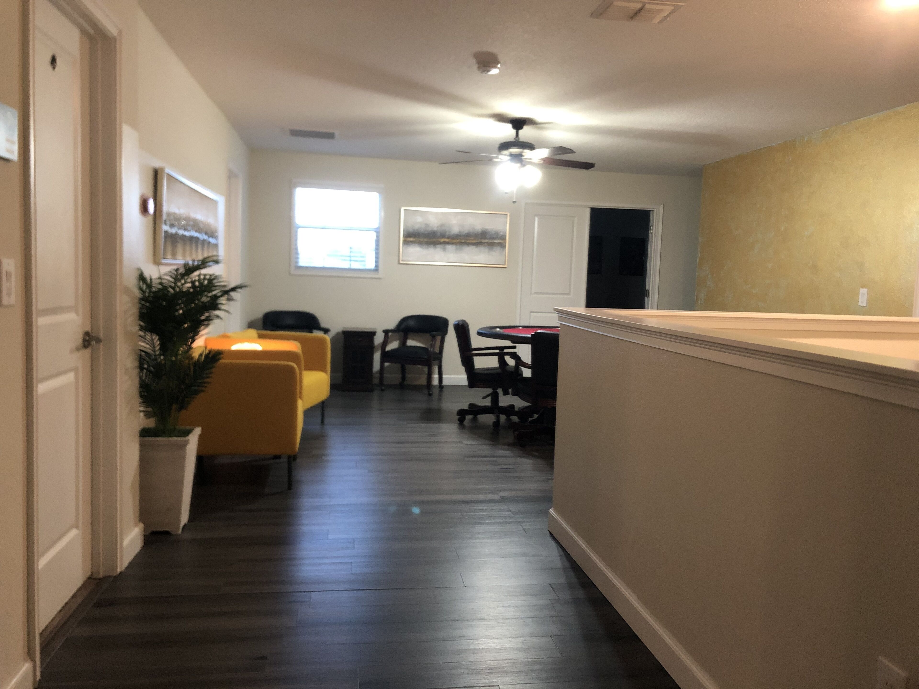 A hallway leading to a dining area with a ceiling fan, a potted plant, and a view of the dining area.