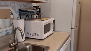 Eine Küche mit einem Edelstahl-Spülbecken, einer weißen Mikrowelle und einem weißen Kühlschrank.