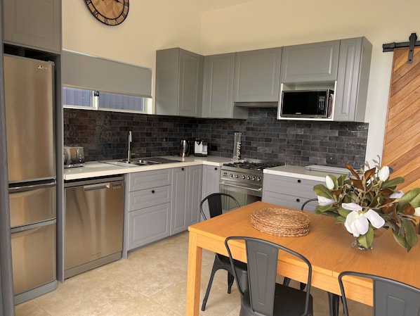 Eine moderne Küche mit grauen Schränken, Edelstahlgeräten, einer Mikrowelle und einem Essbereich mit Holztisch und Stühlen.