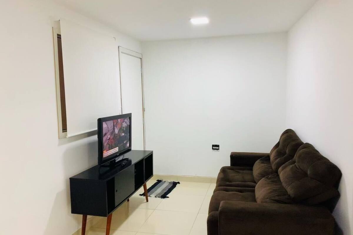 Una sala de estar con un mueble negro para entretenimiento, un sofá marrón y un televisor sobre el mueble.