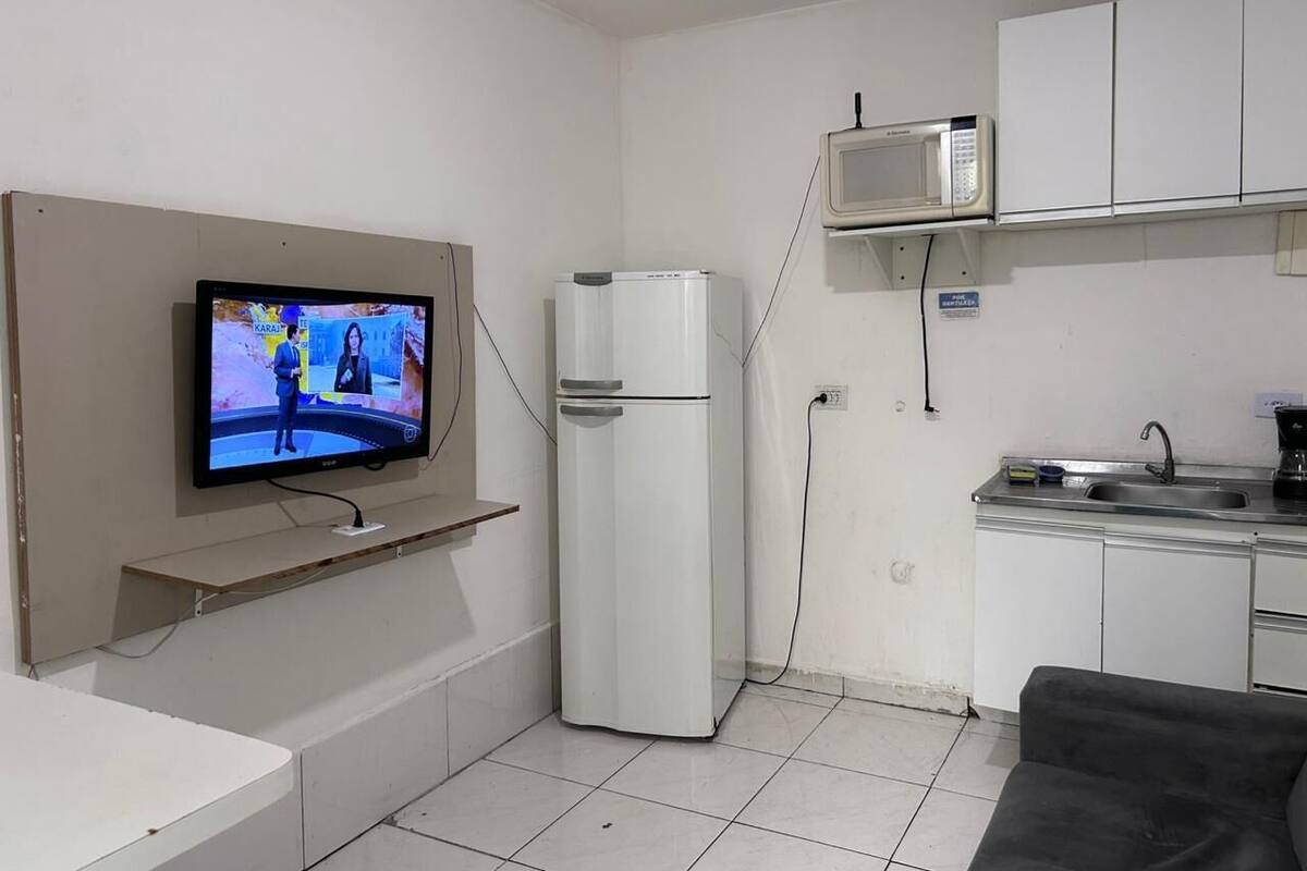 Una cocina compacta con microondas integrado, un refrigerador y un televisor montado en la pared.