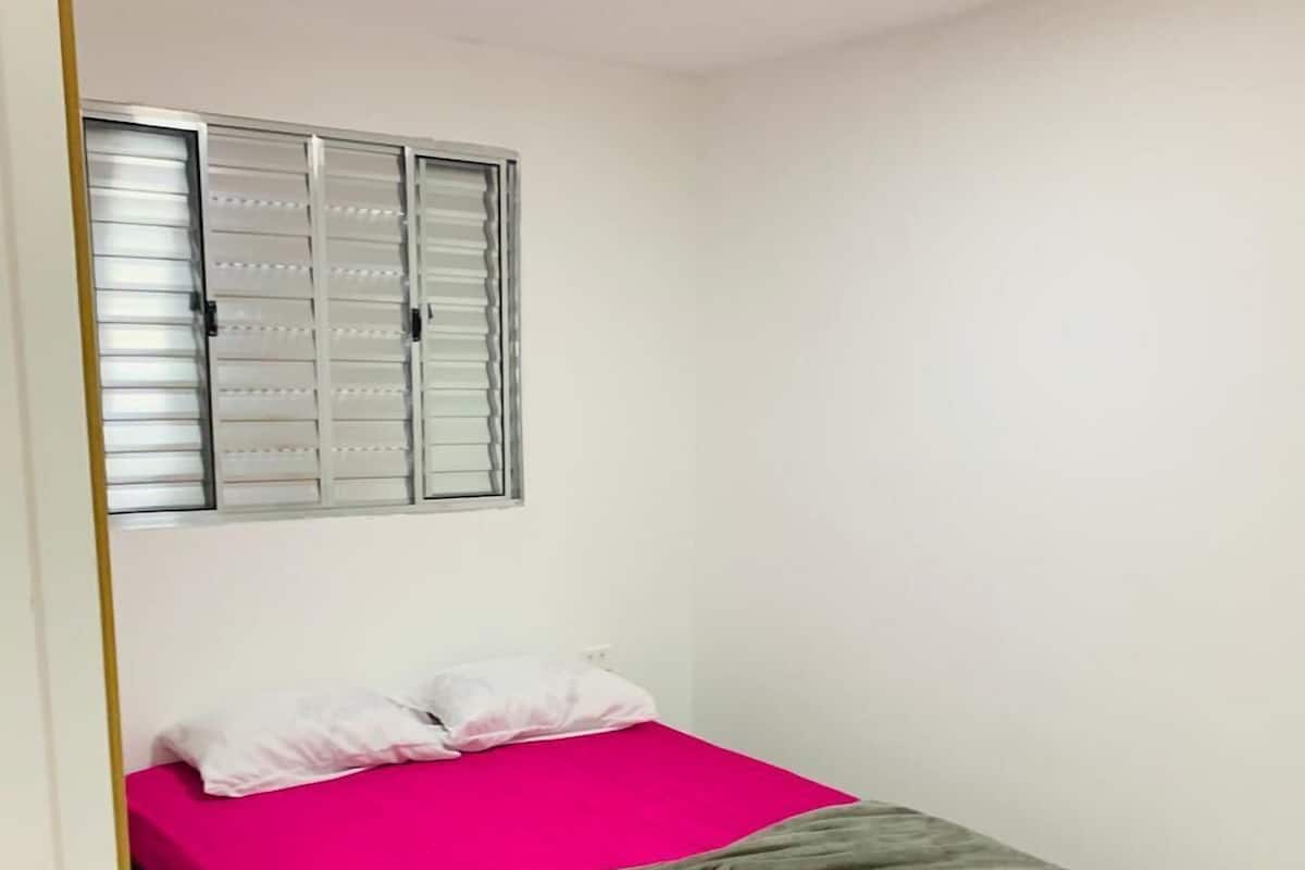 Un dormitorio con cama, ventana con persianas y puerta.