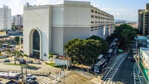 A modern building with a large arched entrance, surrounded by a parking lot and a busy street. - Apartamentos / Studios / Flats em São Paulo Zona Norte Tremembé (São Paulo)