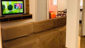 A modern living room with a flat-screen TV, a sofa, and a dining area with a table and chairs. - Apartamentos / Studios / Flats em São Paulo Zona Norte Tremembé (São Paulo)