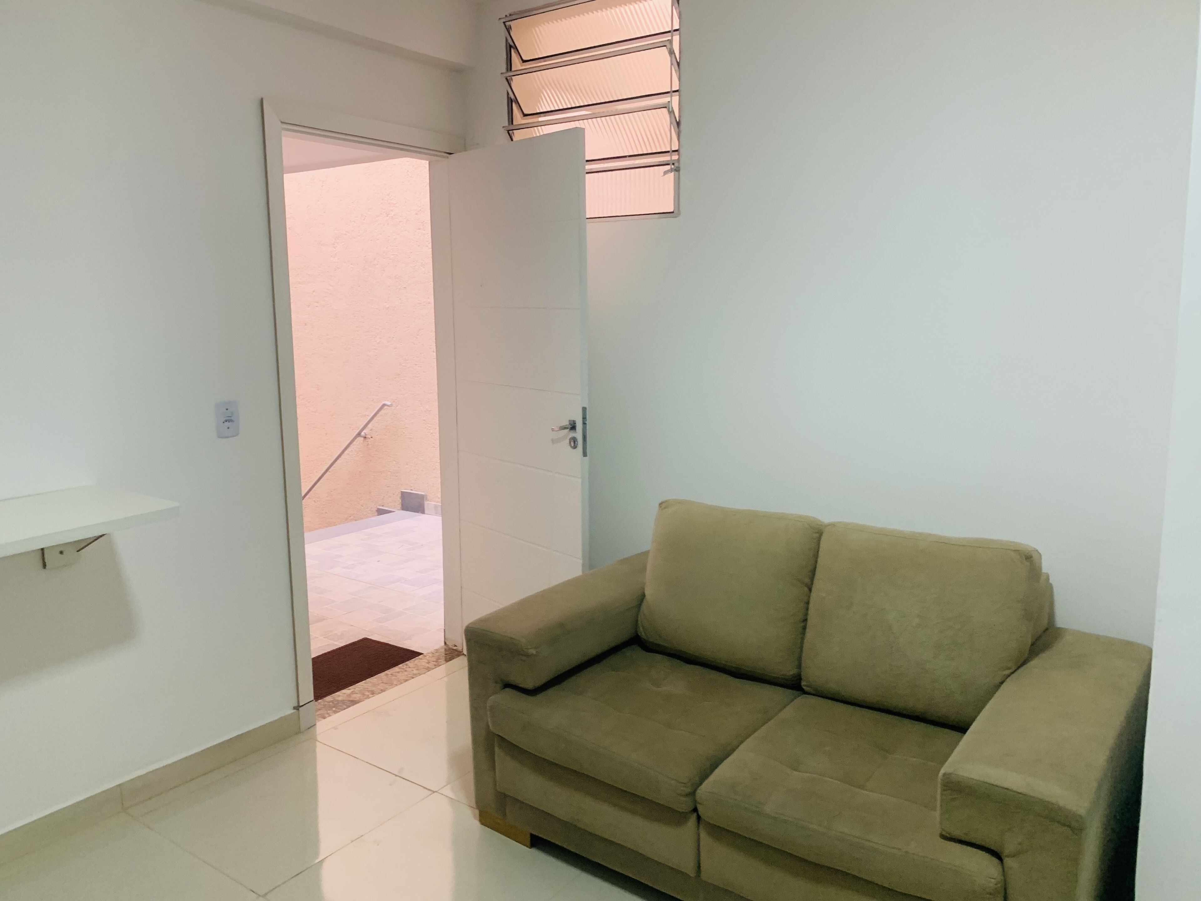 Una habitación con un sofá color beige, una puerta blanca y un estante pequeño.