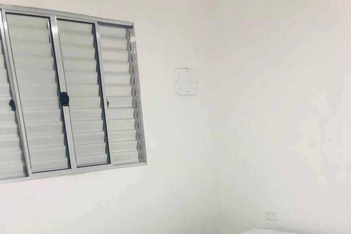 Habitación con una cama individual, colchón blanco y estructura negra, además de una ventana con persianas.