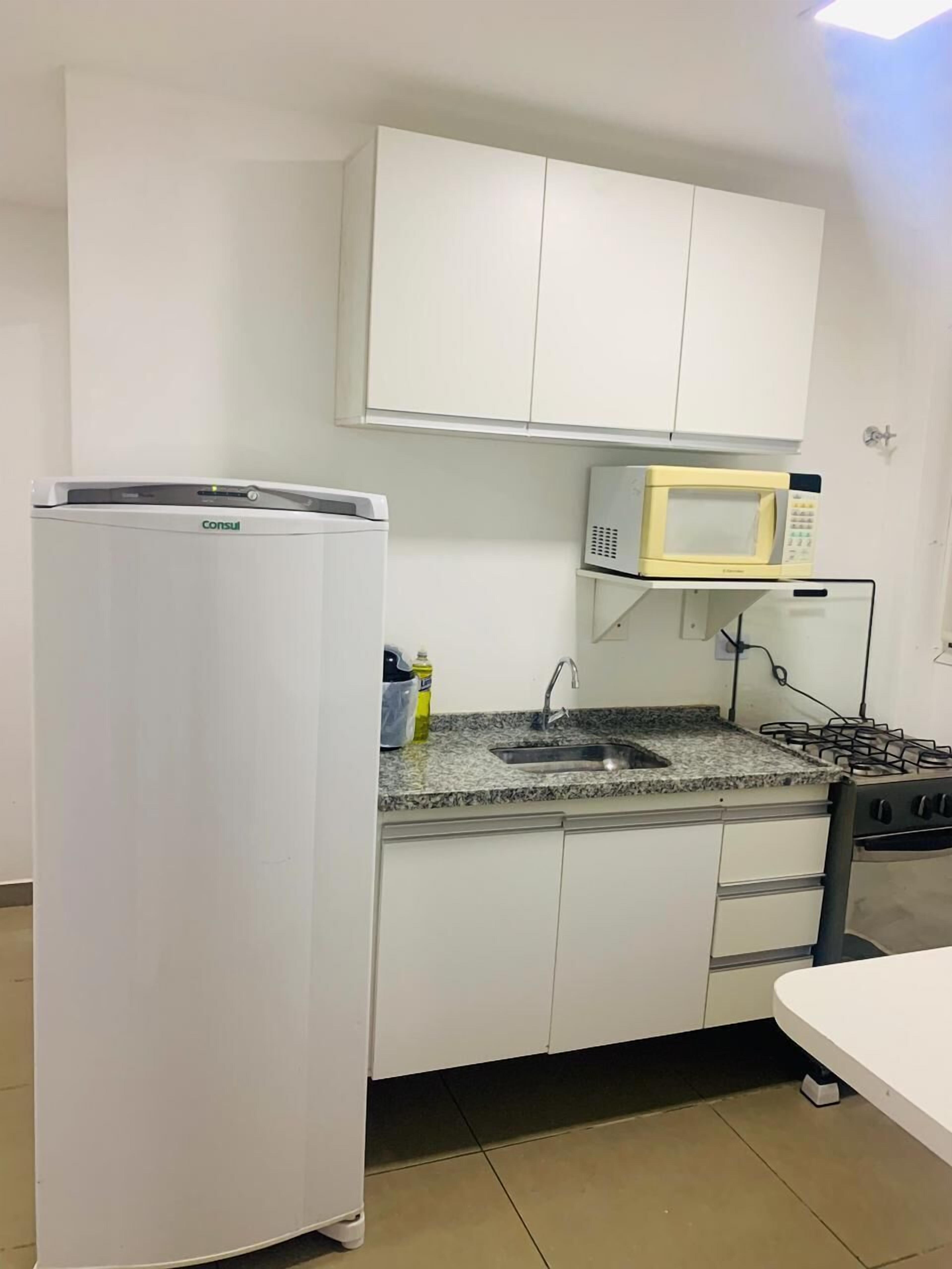Une cuisine compacte avec des meubles blancs, un four à micro-ondes encastré, une cuisinière à gaz et un réfrigérateur.