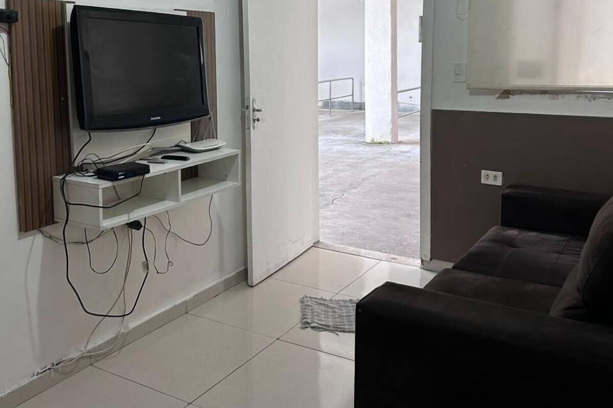 Una sala de estar con un televisor sobre un mueble blanco, un sofá marrón y una puerta que da a un balcón.