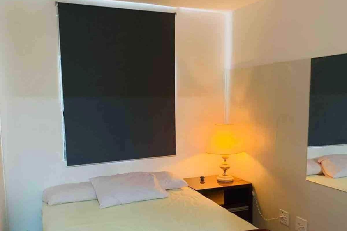 Un dormitorio pequeño y ordenado con una cama individual, una mesita de noche con lámpara y un espejo grande en la pared.