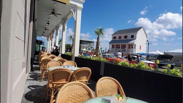 Un espace extérieur aménagé avec des chaises et des tables en osier, une enseigne indiquant « Thorny Oyster Bay St. Louis », et une vue sur la rue, avec des voitures garées et un bâtiment en arrière-plan.