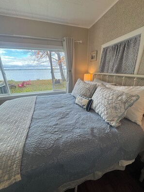 A bedroom with a large bed, a view of the lake, and a chair outside the window. - Charming cottage on Chaumont Bay, pet friendly, kayaks, dock, ICE FISHING (Chaumont)