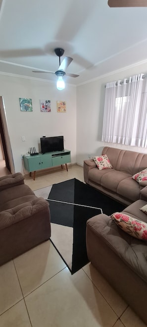 Una sala de estar con un sofá marrón, un aparador verde azulado, un tapete negro y un ventilador de techo.