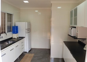 Una cocina compacta con armarios blancos, una encimera negra, microondas integrado y dispensador de agua.
