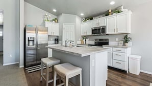 Una cocina moderna con armarios blancos, electrodomésticos de acero inoxidable y una isla central con taburetes de bar.