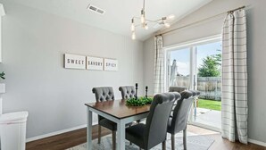 Un comedor con una mesa y sillas, un tapete, una lámpara fijada a la pared y una ventana con cortinas.