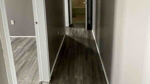 Un couloir étroit doté d’un plancher en bois, de murs blancs et d’un luminaire au plafond.