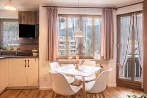 A modern kitchen with a TV, wooden cabinets, and a dining area with white chairs and a table.